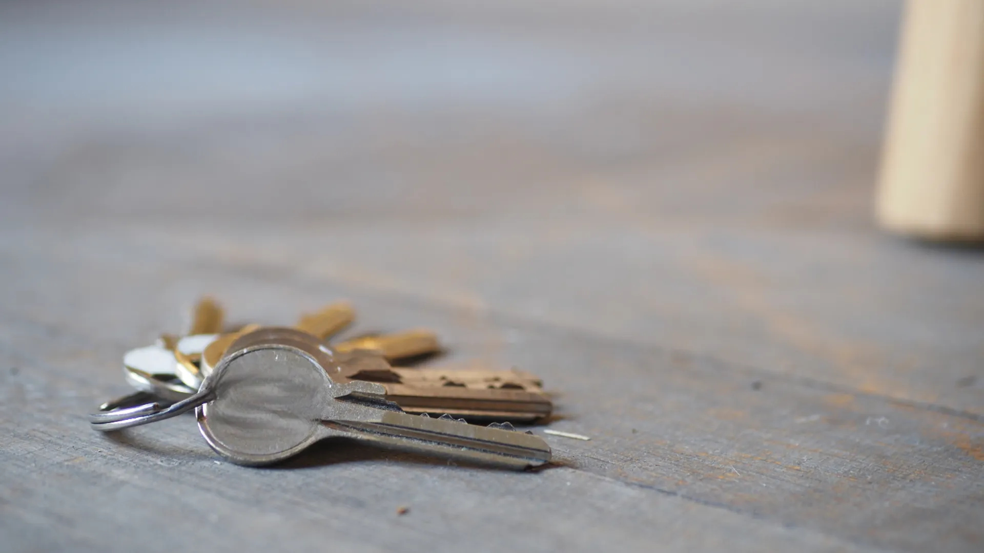 A small bunch of silver keys on a ring lying on a grey wooden surface.