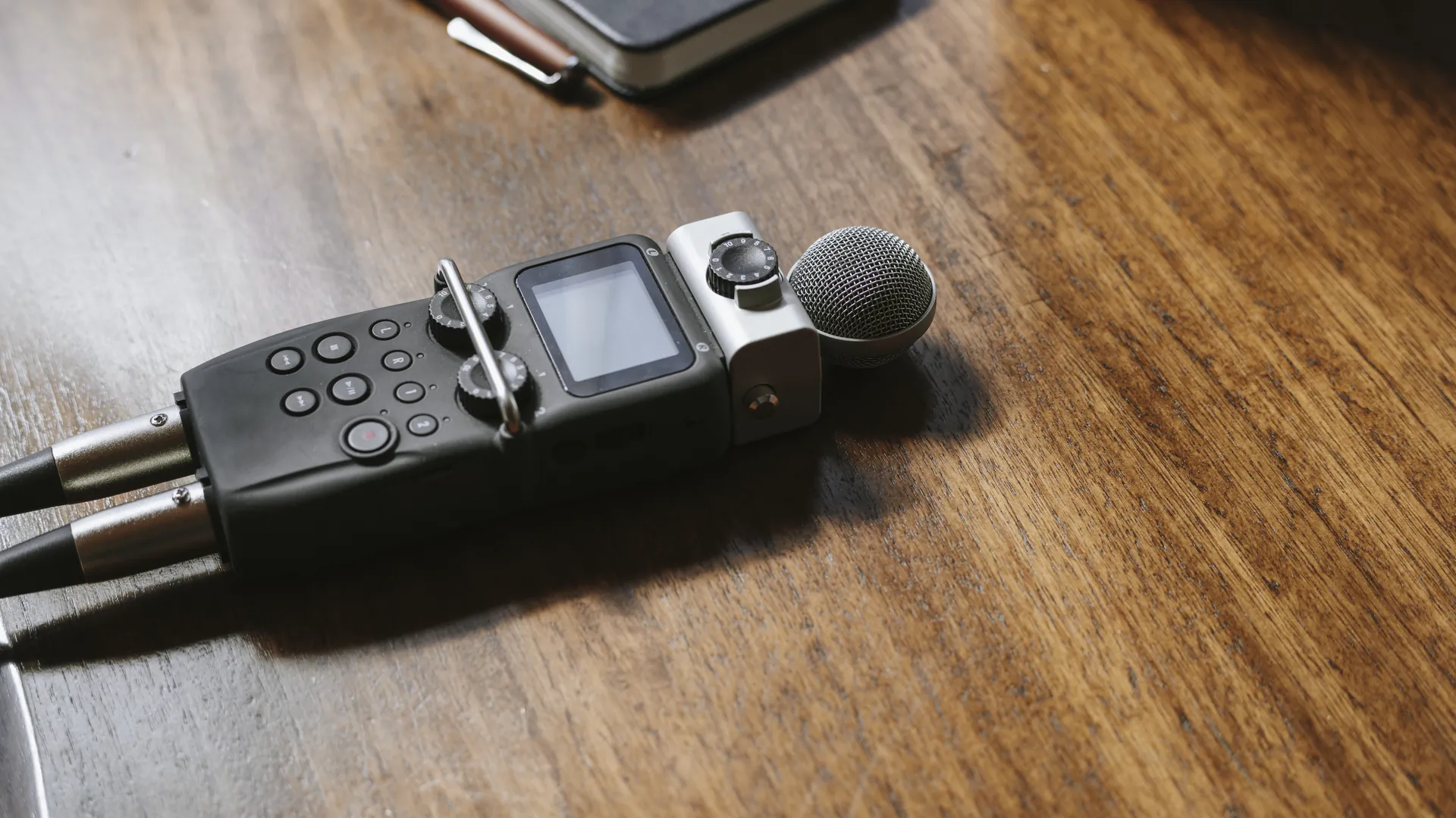A handheld digital audio recorder with a foam-covered microphone lying on a wooden table.