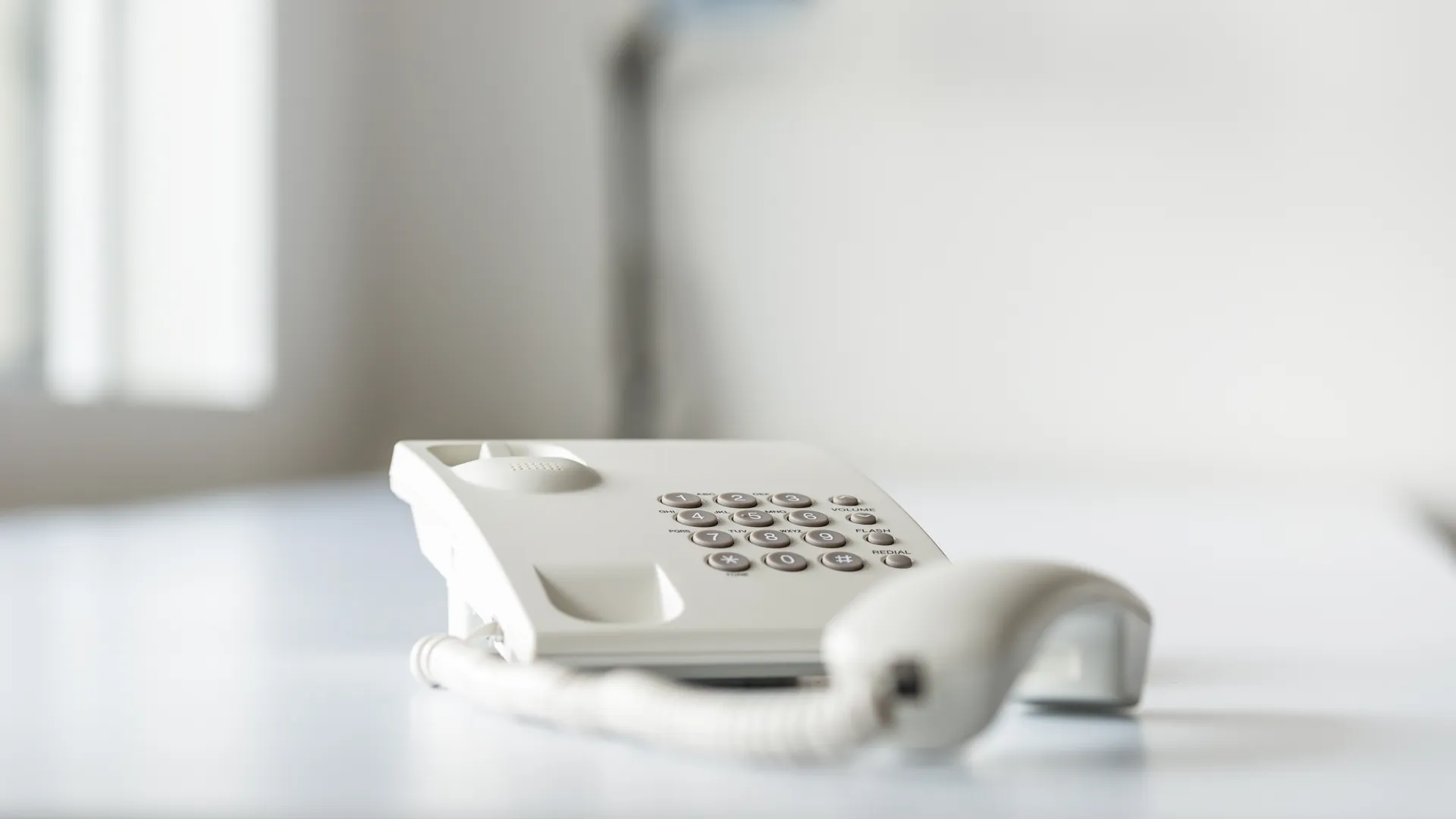 A white landline telephone with its handset off the cradle on a white surface.