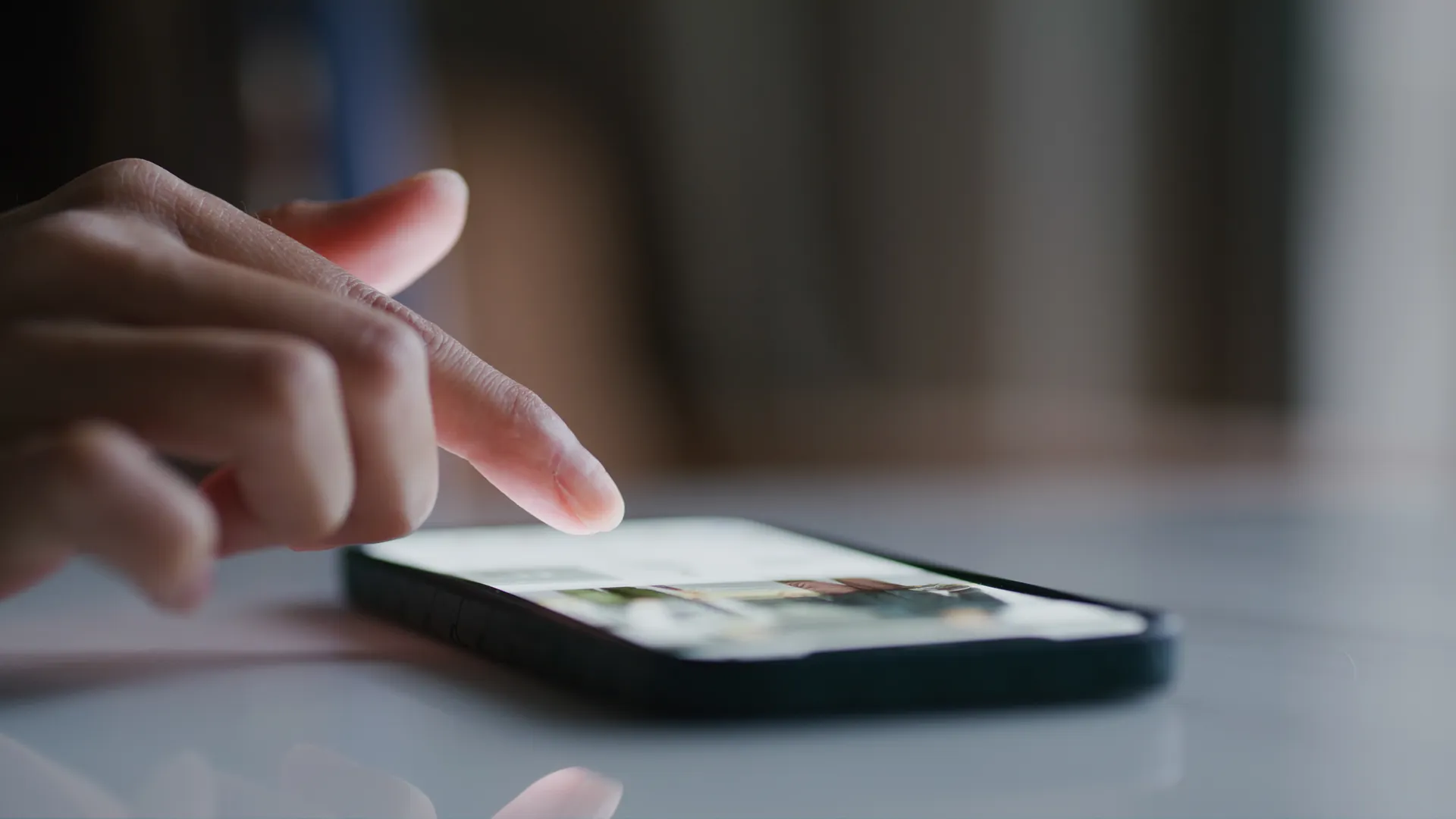 A finger taps the screen of a smartphone lying on a dark glossy surface.