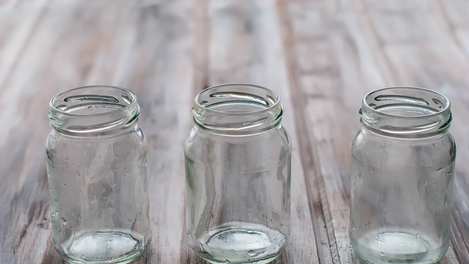 Three empty glass jars stand in a row on a weathered wooden table.