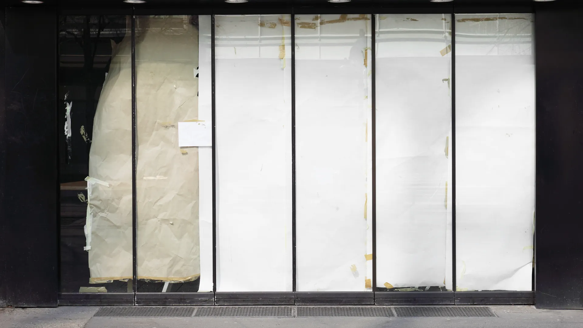 The papered-over windows of a closed shopfront, with crumpled paper taped across the glass.