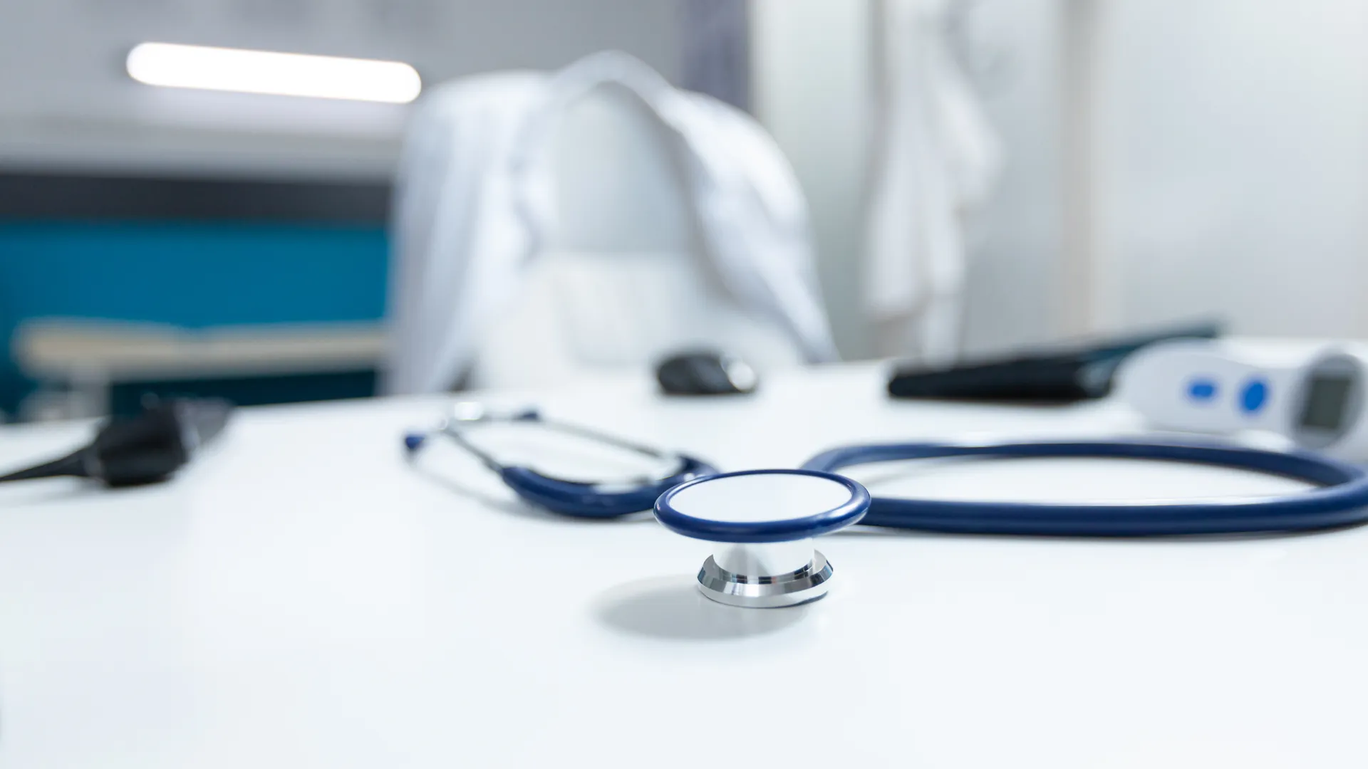 A stethoscope, thermometer and other equipment resting on a white desk in a doctor's office.