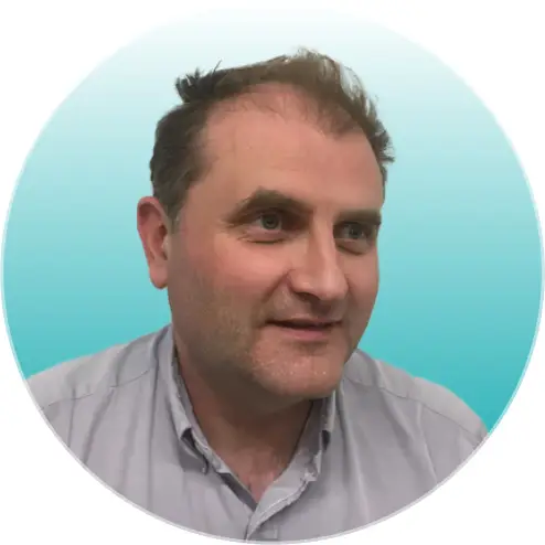 A man with short brown hair and light skin smiles gently, looking slightly to his left. He wears a light grey collared shirt. The background is a smooth gradient of light blue to white, ideal for a healthcare SEO or medical SEO agency profile image.