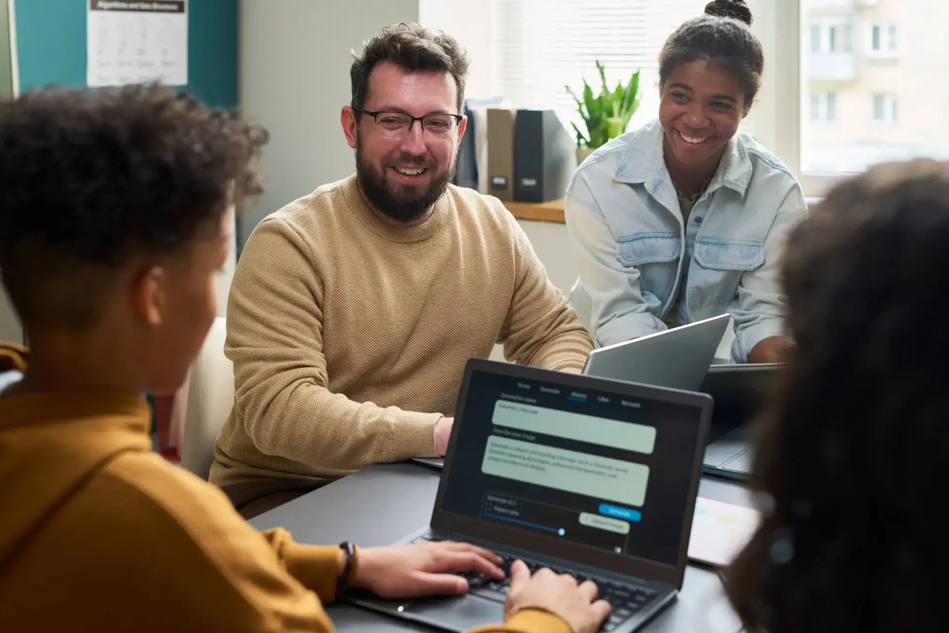 Four people sit around a table in a brightly lit office, talking and smiling. Two laptops, one showing a chat interface, hint at their work for a healthcare SEO agency. Papers and folders are on the table, creating a collaborative atmosphere.