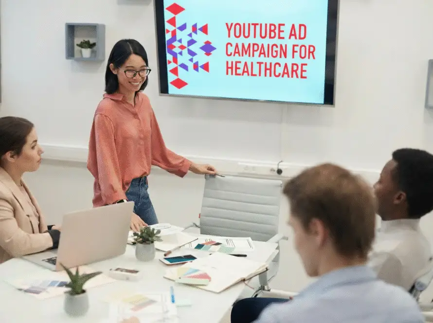 A woman stands presenting to three colleagues in a modern meeting room. The screen displays “YOUTUBE AD CAMPAIGN FOR HEALTHCARE,” reflecting a collaborative strategy session with a leading healthcare digital marketing agency.