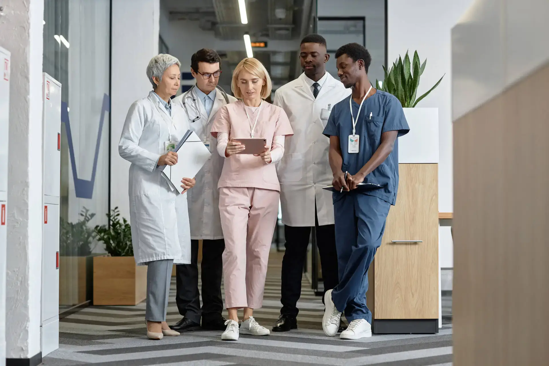 Five medical professionals stand in a corridor, discussing together. Surrounded by modern office décor and plants, they reflect the collaborative spirit of a healthcare digital marketing agency dedicated to innovation in the medical field.