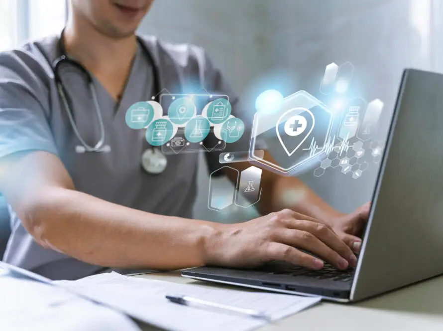 A healthcare worker in scrubs, with a stethoscope round their neck, types on a laptop. Medical-themed digital icons and holograms float above the laptop, highlighting digital health and the impact of a healthcare SEO consultant.