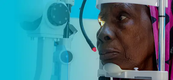 An older person with deep wrinkles undergoes an eye examination, resting their chin on a support while a machine shines a light into their eye. The background features blue gradients and part of the ophthalmology equipment, perfect for medical marketing agency visuals.