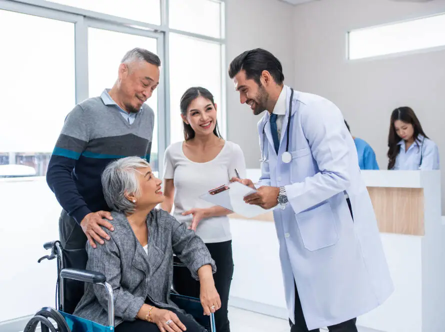 A doctor smiles whilst talking to an elderly woman in a wheelchair, accompanied by a man and a young woman. They appear happy and engaged—a perfect scene for a Healthcare Marketing Agency to highlight compassionate care in a bright medical practice.