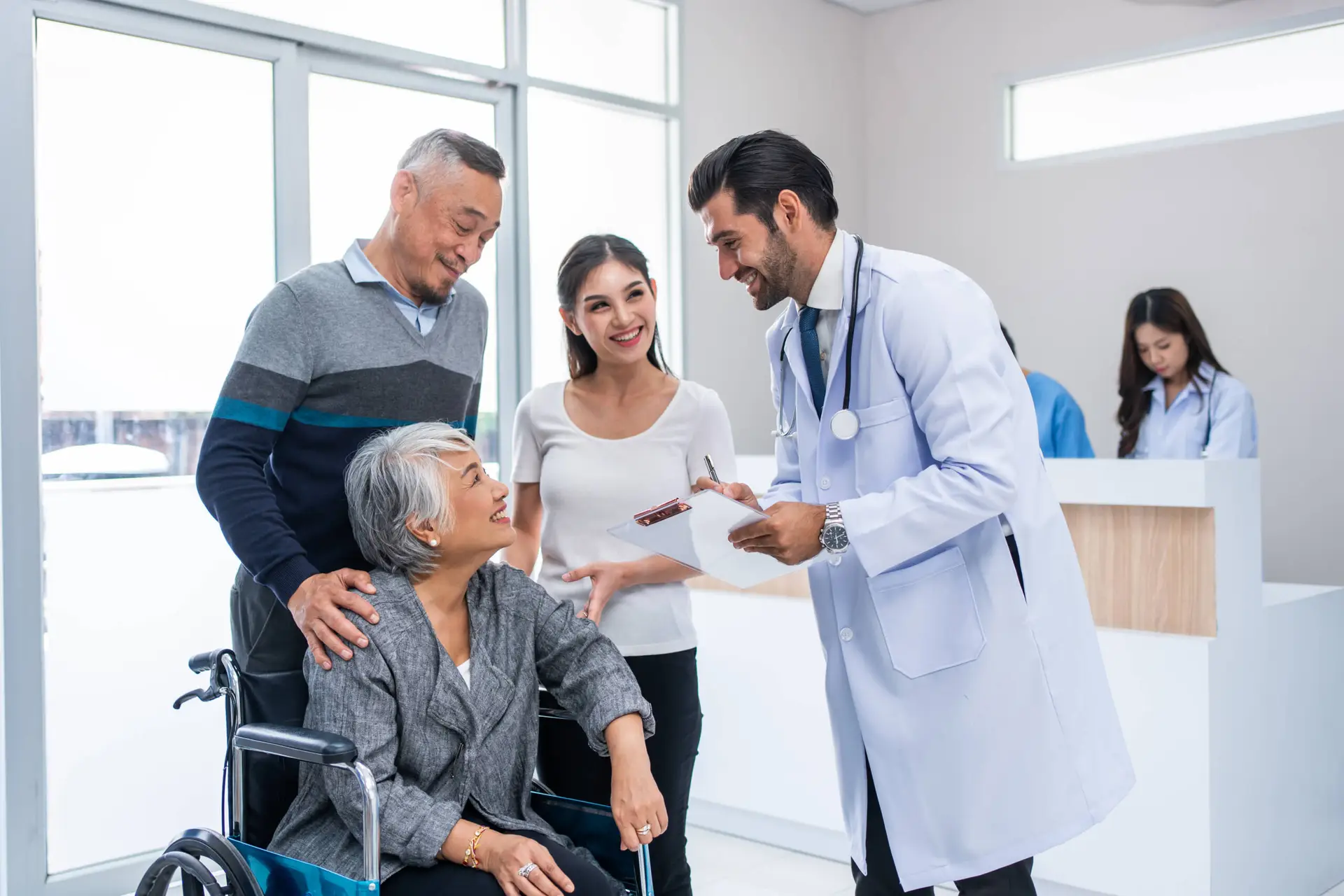 A doctor smiles whilst talking to an elderly woman in a wheelchair, accompanied by a man and a young woman. They appear happy and engaged—a perfect scene for a Healthcare Marketing Agency to highlight compassionate care in a bright medical practice.