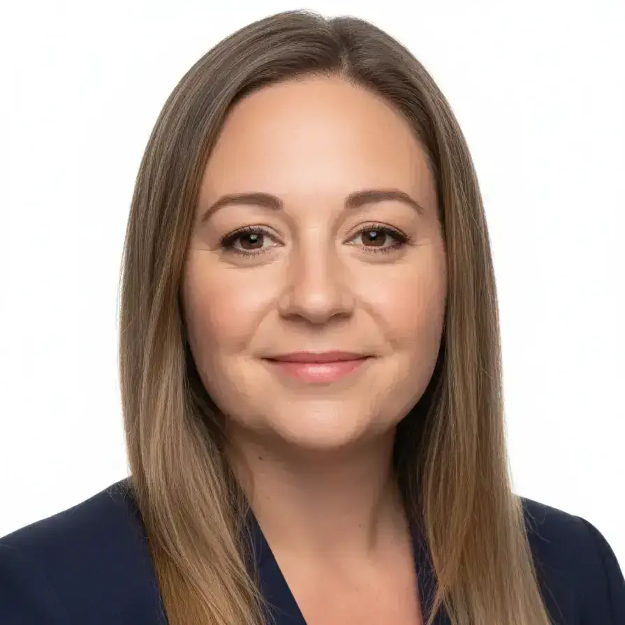 A woman with straight, light brown hair parted to the side, wearing a navy blazer. Emma Fitzsimmons has fair skin and is smiling gently, facing forwards. The plain white background gives the image a professional, portrait style.